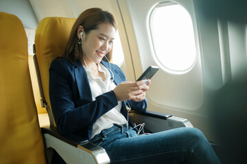 Business woman In a plane, works on using on phone, headphones.