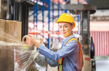 Female worker wrapping boxes in stretch film at warehouse, Worker wrapping stretch film parcel on...