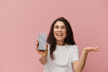 Naklejka premium a beautiful, happy woman in a light t-shirt holds out her phone to the camera showing the screen. Horizontal photo on a plain background with empty space for an advertising insert