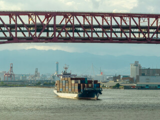 Naklejka premium Container ship with no logos enters harbor under bridge