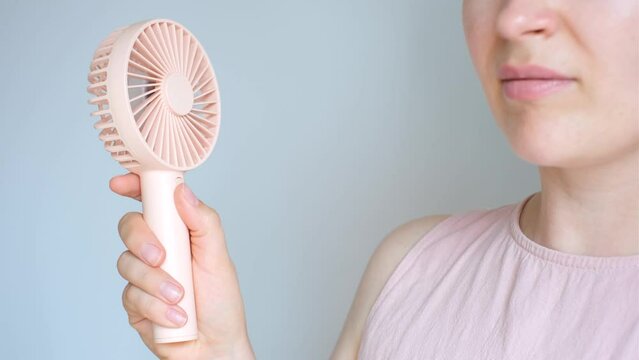 Woman holding pink mini fan close up side view.