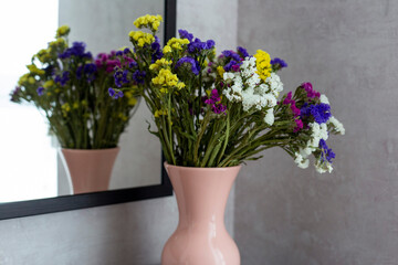 Multi-colored bouquet of dried flowers stand in a pink vase. A bouquet of flowers is reflected in the mirror. Flowers in a pink vase
