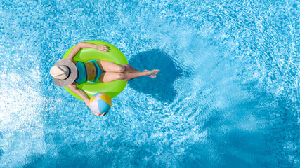Active young girl in swimming pool aerial drone view from above, teenager relaxes and swims on inflatable ring donut and has fun in water on family vacation, tropical holiday resort
