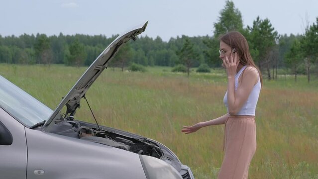 Angry young woman checking her broken car in nature. Call by phone.