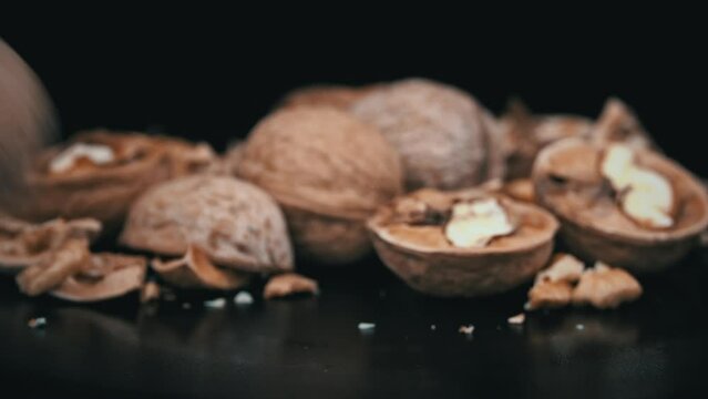 Whole walnut rolls in slow motion against a background of pile of nuts in a loop. A lot of walnuts in the shell rotate on a black background. Nuts are good for the brain. Heap of walnuts close-up.