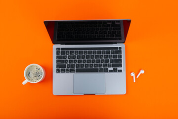 Laptop with blank screen, cup of coffee and wireless headphones on orange background