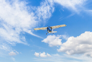 Single engine ultralight plane flying in the blue sky with white clouds