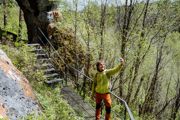 A tourist takes a selfie against the background of nature standing on an iron staircase in the mountains, a national park, a pedestrian road for tourists, a hike in the forest, a photo.