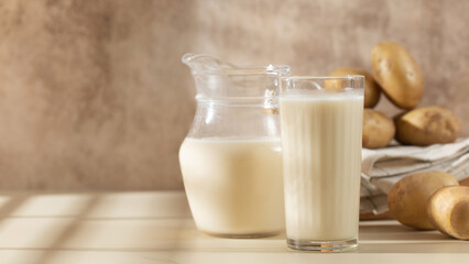 A glass and a jug of potato milk with raw potatoes in a bowl. Copy space