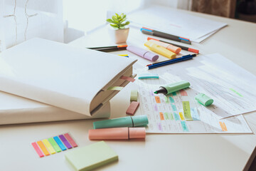 The process of planning the school week. Student workplace with scattered markers, books in white covers. Selective focus. Side view. A real workplace.