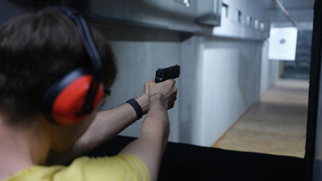 Guy in tactical headphones aiming pistol at target in shooting range