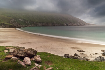 Fototapeta na wymiar Keem bay and beach. Achill island, county Mayo, Ireland. Low clouds over ocean and mountains. Popular tourist area with stunning nature scenery and clean blue water and sandy beach