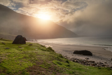 Two tents set up on a green grass patch of land. Mountain in the background. Travel and tourism concept. Campsite in nature area. Beautiful sun rises over a mountain. Keem beach, Ireland. Calm mood.