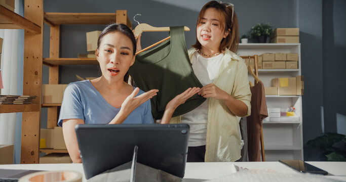 Professional attractive cheerful two young Asian successful lady owner teenage partner with casual live streaming on tablet show new collection produce to customer. New business start up concept.