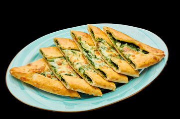 Turkish pizza pide with spinach and cheese lies on a plate on a black isolated background