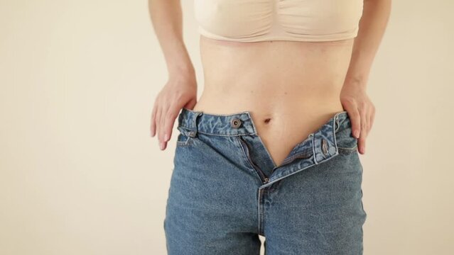 A young woman mother unbuttons her jeans and shows her scar from a cesarean section. Body positivity. diversity. Light warm natural tones. Lifestyle.