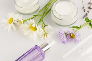 Jars with organic creams, bottle with serum and wild flowers on a white background. Concept of wild-harvested beauty and natural cosmetics based on a wild plant. Soft focus style