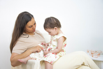 Mom and daughter are sitting against the background of a white wall, looking at flowers on a dress