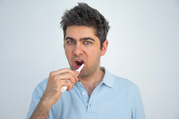 A man in a blue t-shirt with tousled hair brushes his teeth
