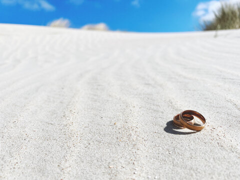 Rose gold wedding  rings jewelry  at the beach, lots of copy space on the sand. Summer wedding background.