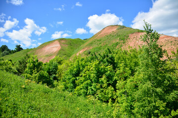steep clay hills covered with green grass with blue sky and clouds on background
