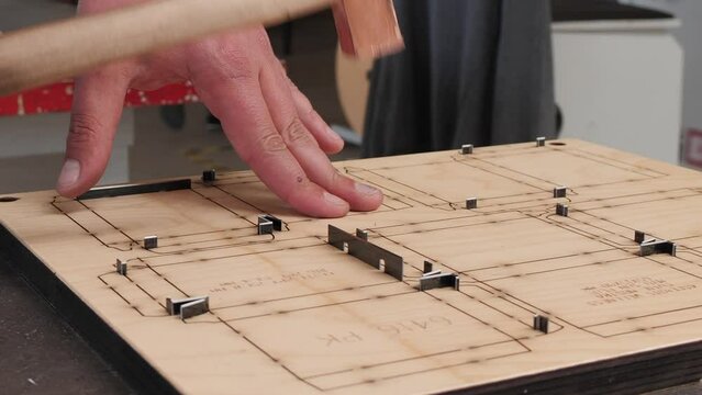 Manufacturing die cutter plate - close up on worker hand inserting cutting blades in plywood plank slots previously prepared with laser precision cnc machine, camera slide