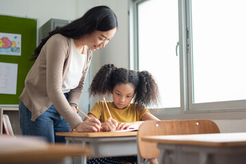 Young Asian Woman Teacher teaching her African American girl in classroom at elementary schoolgirl - obrazy, fototapety, plakaty