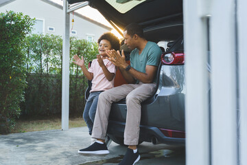 Cheerful Black African Father and little boy having fun sitting in car trunk before Holiday Road...