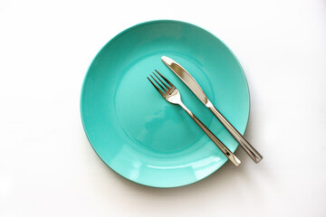 Served plate with cutlery. Empty green plate and stainless knife and fork isolated on white...