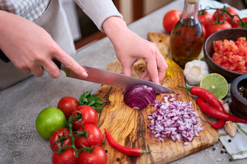woman cutting and chopping onion by knife on wooden board