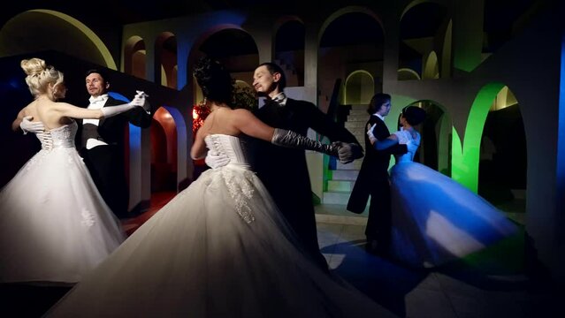 four pairs of beautiful adults are dancing a waltz at the ball. men are dressed in a tailcoat and girls in ballroom long dresses