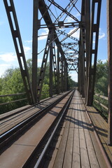 The metal structure of the railway viaduct over the river against the background of a blue sky with clouds.