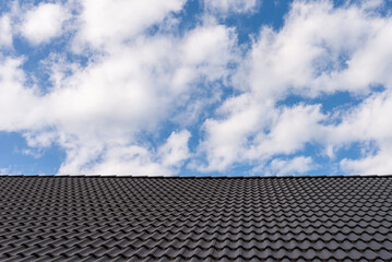 Fototapeta na wymiar Black tile roof against blue sky with white clouds.