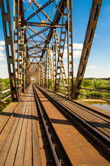 Fototapeta premium The metal structure of the railway viaduct over the river against the background of a blue sky with clouds.