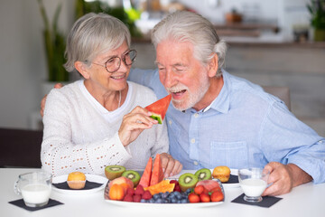 Beautiful caucasian retired senior couple having breakfast at home with fresh seasonal fruit, milk...