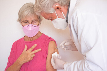Doctor giving injection to senior caucasian woman, female receiving third booster of covid 19...