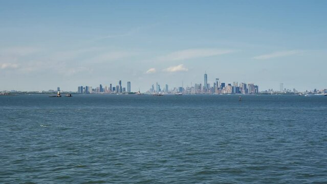 Super wide angle shot of the Financial District of Manhattan, with the One World Trade Center and the Statue of Liberty on a sunny day with blue skies, moving shot.