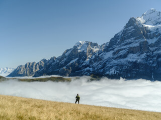 Tourist stands in front of the mountains and clouds in the valley at Grindewald, Switzerland.