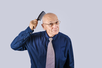Strange mature man holds hair brush on bald head. Male alopecia problem.