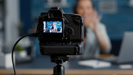 Modern camera filming influencer talking to audience. Popular social media content creator recording vlog for internet video sharing platforms while sitting at studio desk. Close up