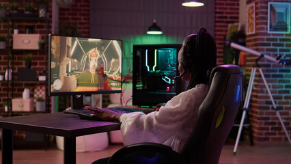 Over shoulder view of woman streaming first person shooter doing victory hand gesture after win in tournament. African american gamer girl surprised after winning online competition on gaming pc. © DC Studio