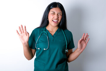 Emotive Doctor hispanic woman wearing surgeon uniform over white wall laughs loudly, hears funny...