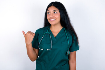 Charming Doctor hispanic woman wearing surgeon uniform over white wall looking at copy space having advertisements