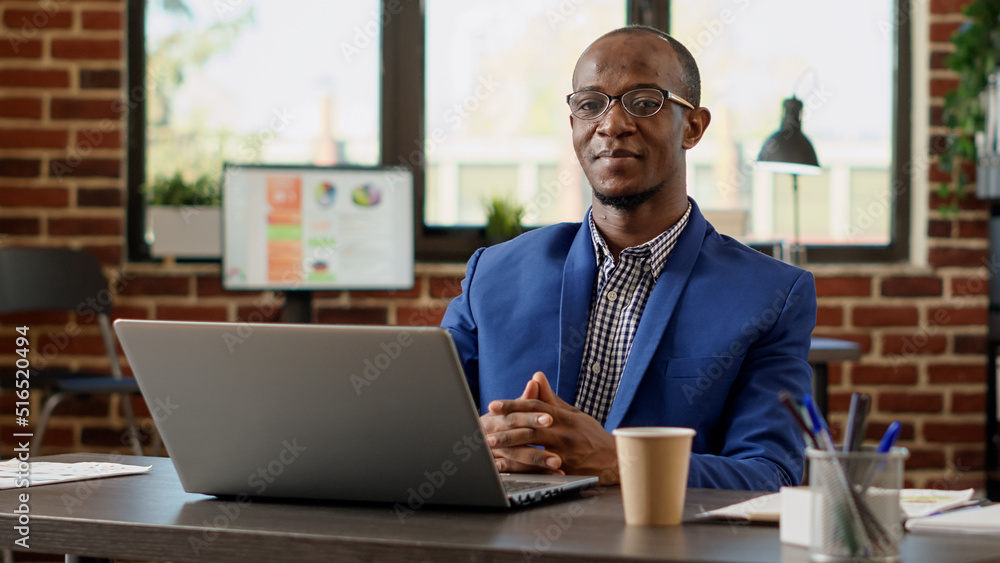 Poster portrait of african american worker sitting at office desk, using laptop to work on executive projec