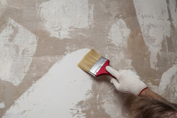 gloved hand with a brush on the background of a putty wall
