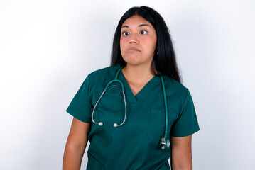 Doctor hispanic woman wearing surgeon uniform over white wall making grimace and crazy face, screaming out of control, funny lunatic expressing freedom and wild.