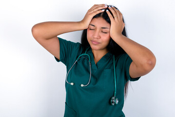 Doctor hispanic woman wearing surgeon uniform over white wall suffering from strong headache desperate and stressed because of overwork. Depression and pain concept.