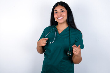 Doctor hispanic woman wearing surgeon uniform over white wall pointing fingers to camera with happy and funny face. Good energy and vibes.