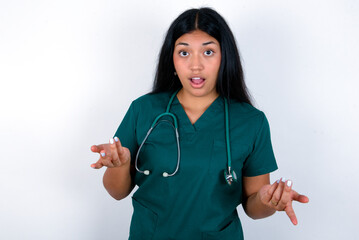 Frustrated Doctor hispanic woman wearing surgeon uniform over white wall feels puzzled and...