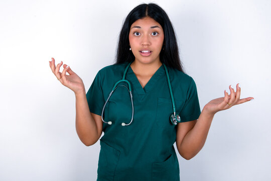 Surprised terrified Doctor hispanic woman wearing surgeon uniform over white Gestures with uncertainty, stares at camera, puzzled as doesn't know answer on tricky question, People, body language, 